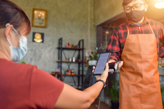 Woman making a contactless payment on a credit card reader with her mobile phone
