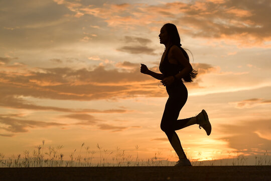 Silhouette of a woman running in countryside at sunset, Thailand