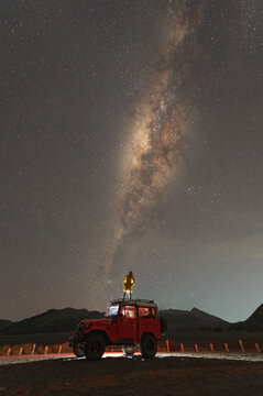 Woman standing on a truck looking at Mt Bromo and milky way, East Java, Indonesia