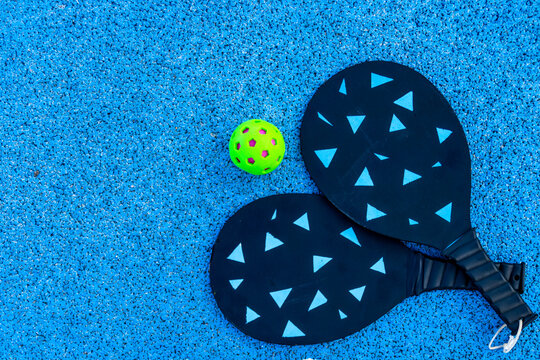 Closeup of a pickleball and paddles on an empty blue court