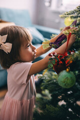 Adorable toddler girl decorating Christmas tree with balls
