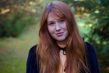 Fototapeta premium Witch young ginger woman in a black robe walks through the forest, the concept of Halloween, esotericism, mysticism, magic, sorcery, pumpkin