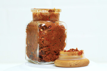 A transparent jar with adjika and a wooden lid on a white table.