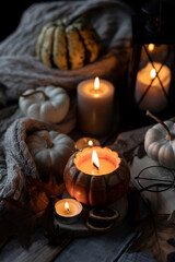 Atmospheric candle - shape of pumpkins, autumn decor, book on grey fall rainy day. Autumn cozy home atmosphere, inspiration, hygge concept. Aromatherapy, warming, relaxation. Wooden background