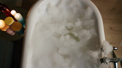 Luxury bathtub foamy water at candles room top view. Bubbles filled bath evening