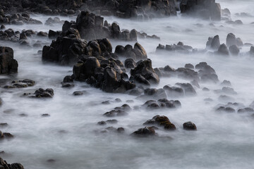 Long exposure view of coastal rocks surrounded by water.