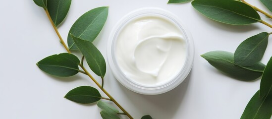 A white cosmetic jar with natural facial cream on white background next to leaves