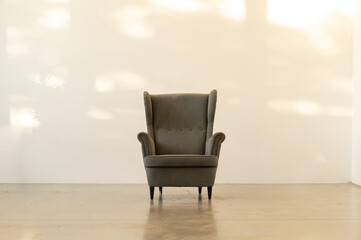 Classic English armchair on the background of an empty wall. Sunset light on the wall.