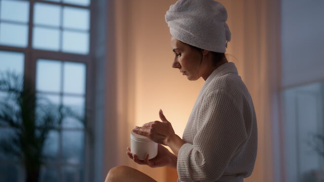 Gorgeous woman moisturizing legs at bath closeup. Lady putting cream at evening