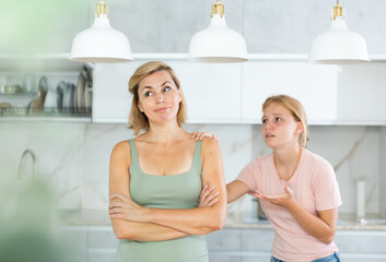 Teenage girl trying to talk and apologize to her offended mother after home disagreements..