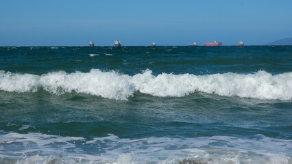 Ocean view from the beach with boats and tankers. Sea harbor, big waves. Storm