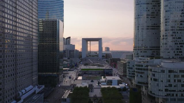 People walking in public place in modern La Defense business district at twilight. Aerial ascending footage of futuristic skyscrapers. Paris, France