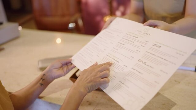 Senior asian female chooses aroma oils from menu at authentic spa. Elderly biracial woman smells fragrance oil in glass bottles at atmospheric retreat facility. Multiethnic adult at beauty center
