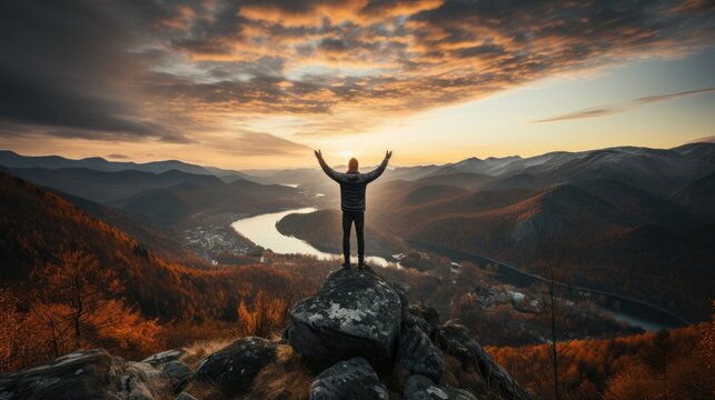 Man raises one hand punching the air on mountain peak with sunset background no face back view