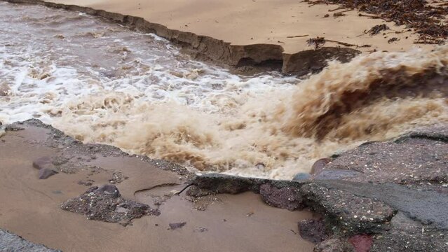 Cascading flood waters from a heavy rain event emitting from a storm drain and on to a beach