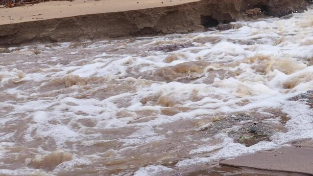 Turbulent flood waters from a heavy rain event emitting on to a beach