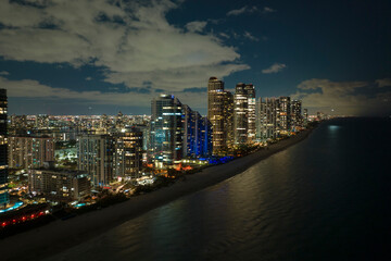 Fototapeta na wymiar Night urban landscape of downtown district in Sunny Isles Beach city in Florida, USA. Skyline with brightly illuminated high skyscraper buildings in modern american megapolis