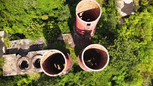 Aerial drone high angle footage of nature reclaiming the area of an abandoned old factory. Top down flyover shot of vintage brick cooling towers overgrown by plants. Top down shot. Old and industrial.