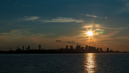 Naklejka premium Silhouette of Boston from Boston Harbor with an airplane coming in for a landing