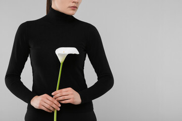 Woman with calla lily flower on light grey background, closeup and space for text. Funeral ceremony