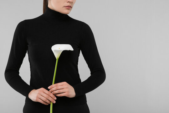 Woman with calla lily flower on light grey background, closeup and space for text. Funeral ceremony - Powered by Adobe