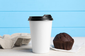 Paper cup with black lid and muffin on white wooden table. Coffee to go