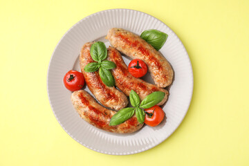 Plate with tasty homemade sausages, basil leaves and tomatoes on yellow table, top view