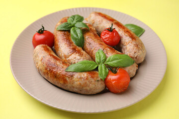 Plate with tasty homemade sausages, basil leaves and tomatoes on yellow table, closeup