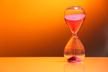 Hourglass with flowing sand on color background. Space for text
