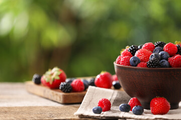 Bowl and different fresh ripe berries on wooden table outdoors, space for text