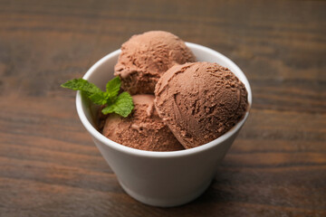 Bowl with tasty chocolate ice cream and mint leaves on wooden table