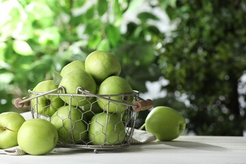Metal basket with ripe green apples on white table outdoors, space for text
