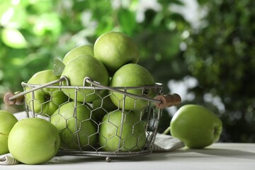 Metal basket with ripe green apples on white table outdoors. Space for text