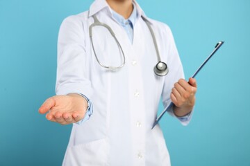 Doctor with stethoscope and clipboard holding something on light blue background, closeup