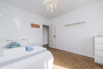 Fototapeta na wymiar A room with a double bed with a white bedspread, some towels and cushions. White lacquered access door and smooth white painted walls