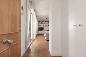 Hall of an apartment with a white built-in wardrobe and direct access to a living room with plain white painted walls.