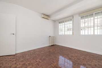 Empty room with white doors, windows with bars, air conditioner and cast iron radiator