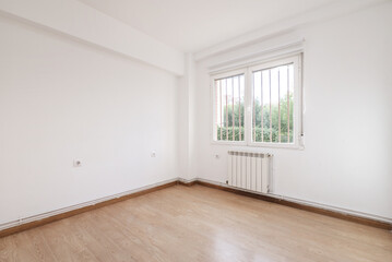 Empty room with barred windows, light-colored wooden floors, aluminum radiator under the window and white painted walls