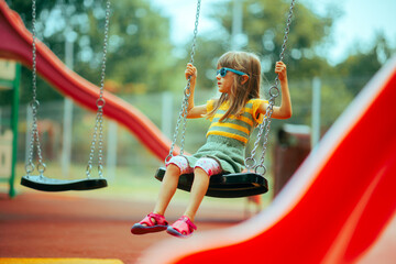 Little Toddler Girl Playing in a Swing at the Playground. Child having fun by herself playing independently. 
