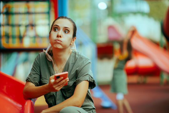 Tired and Bored Mom Spending time on her Phone at the Playground. Mother overusing technology while babysitting in the park 
