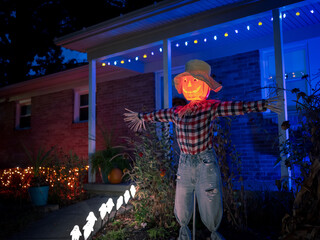 Pumpkin head scarecrow in front of house decorated for Halloween