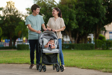 happy parent (father and mother) talking and pushing infant baby stroller and walking in park