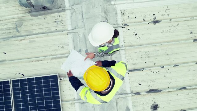 Engineer, safety and planning for solar with top view of installation, teamwork and blueprints for design on roof. Construction worker, electrician and maintenance for power of building with panel
