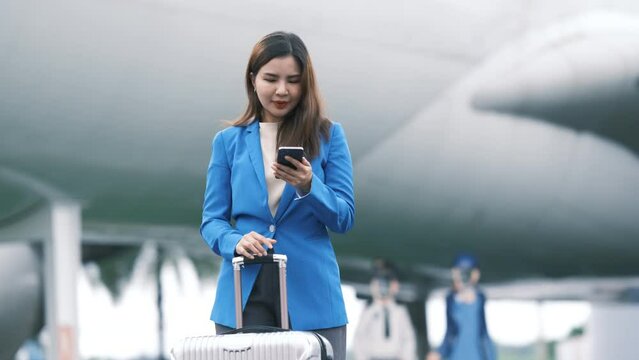 Asian businesswoman uses mobile phone while inside the airport, Asian tourist female wearing suit pull trolley bag. Businesswoman Travel concept.