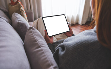 Mockup image of a woman holding digital tablet with blank desktop screen while lying on a sofa at...