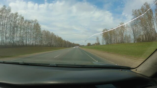 First-person view through the windscreen of a car on the road. Rural single lane road. A crack in the windscreen. Travelling by car