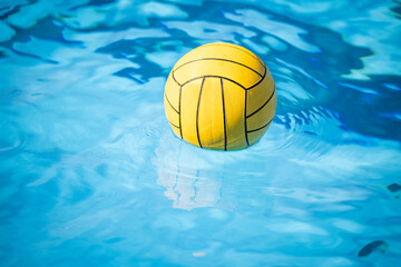 A yellow water polo ball floating in a swimming pool