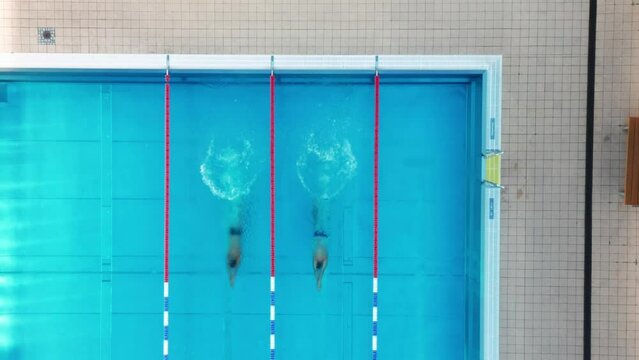 Top-down static drone shot of 2 swimmers swimming along a swimming pool
