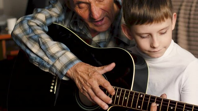 Grandson and grandfather playing the guitar at home, old man is teaching a boy to play. Musical instruments and lifestyle concept.