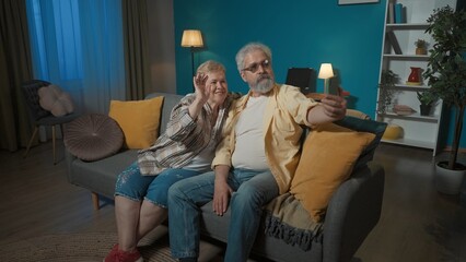 In the picture, an elderly couple is sitting on a sofa in a room. The man is holding a phone on his arm. The woman snuggled up against the man and both look at the phone. Demonstrate photo posing - Powered by Adobe